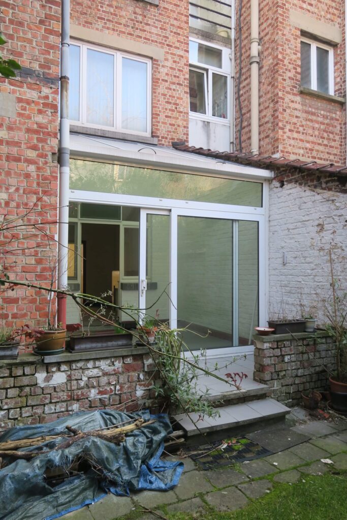 véranda construite entre un mur mitoyen et une annexe avec accès à une terrasse et jardin