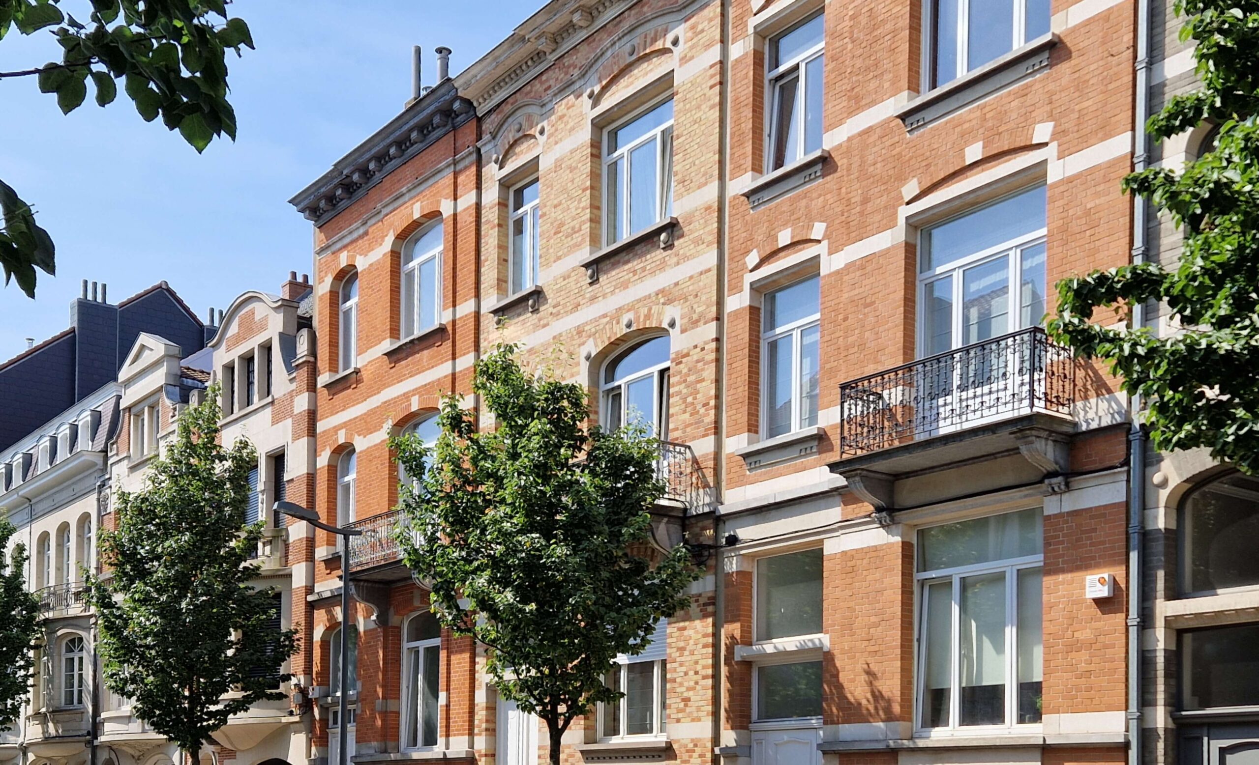 Trois maison en briques de couleur orange avec châssis blanc et arbre planté en voirie. VMAR, architecte spécialisé dans la régularisation des infractions urbanistiques à Bruxelles.